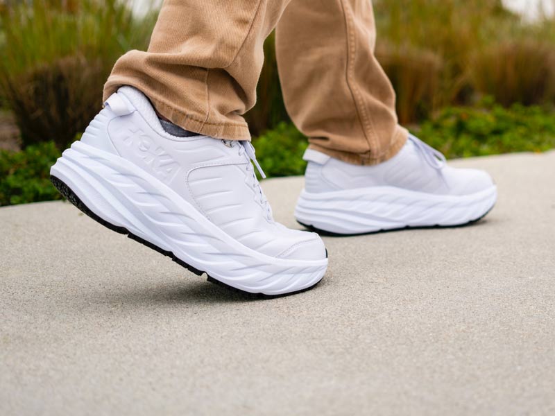 Man walking down sidewalk wearing HOKA shoes.
