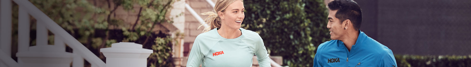 Woman and mann running through neighborhood in HOKA athletic apparel