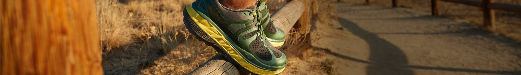 Person standing on wooden fence wearing HOKA shoes.
